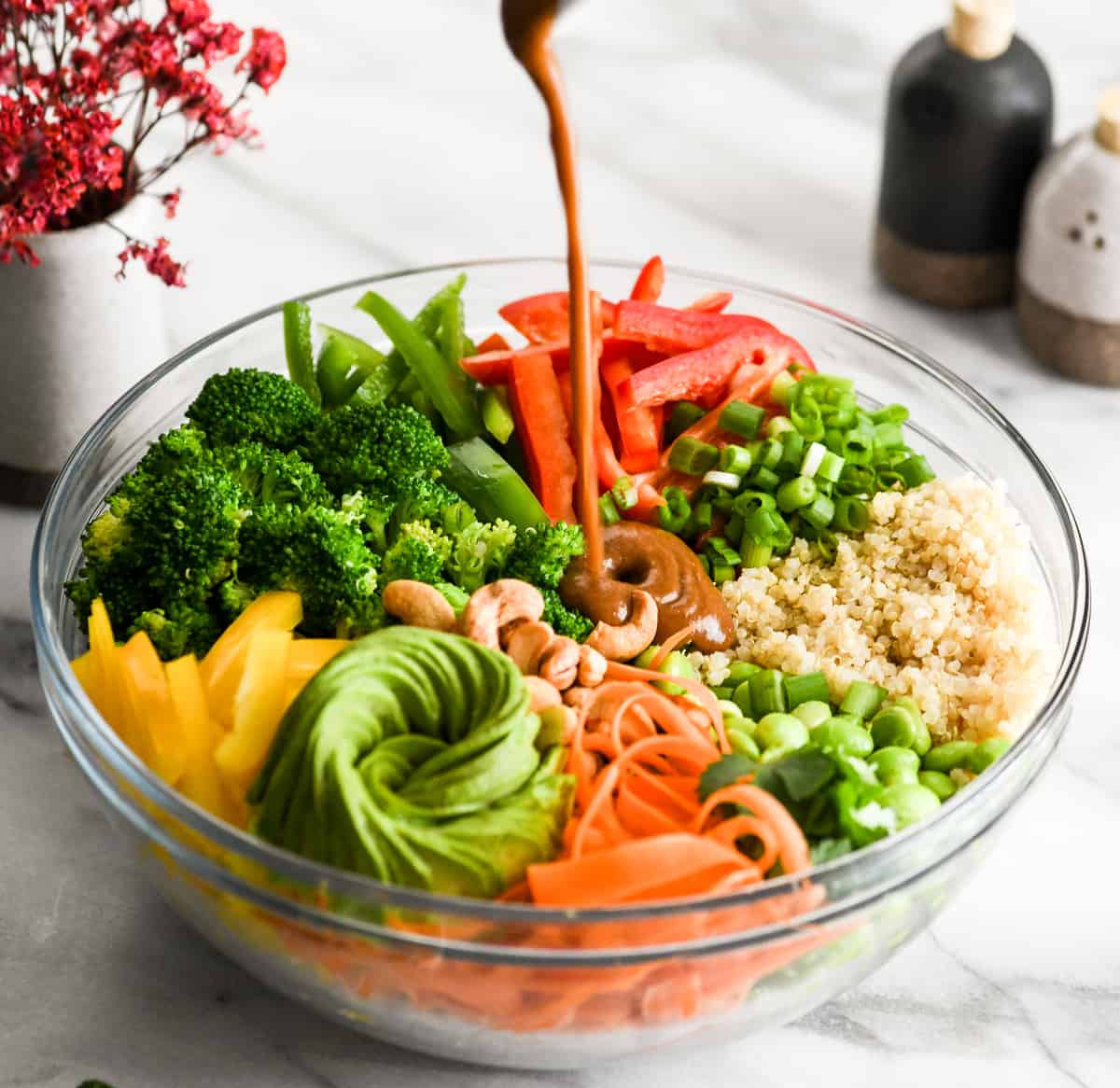 Side view of Peanut sauce being poured into a bowl with all the ingredients of asian quinoa salad with peanut dressing recipe