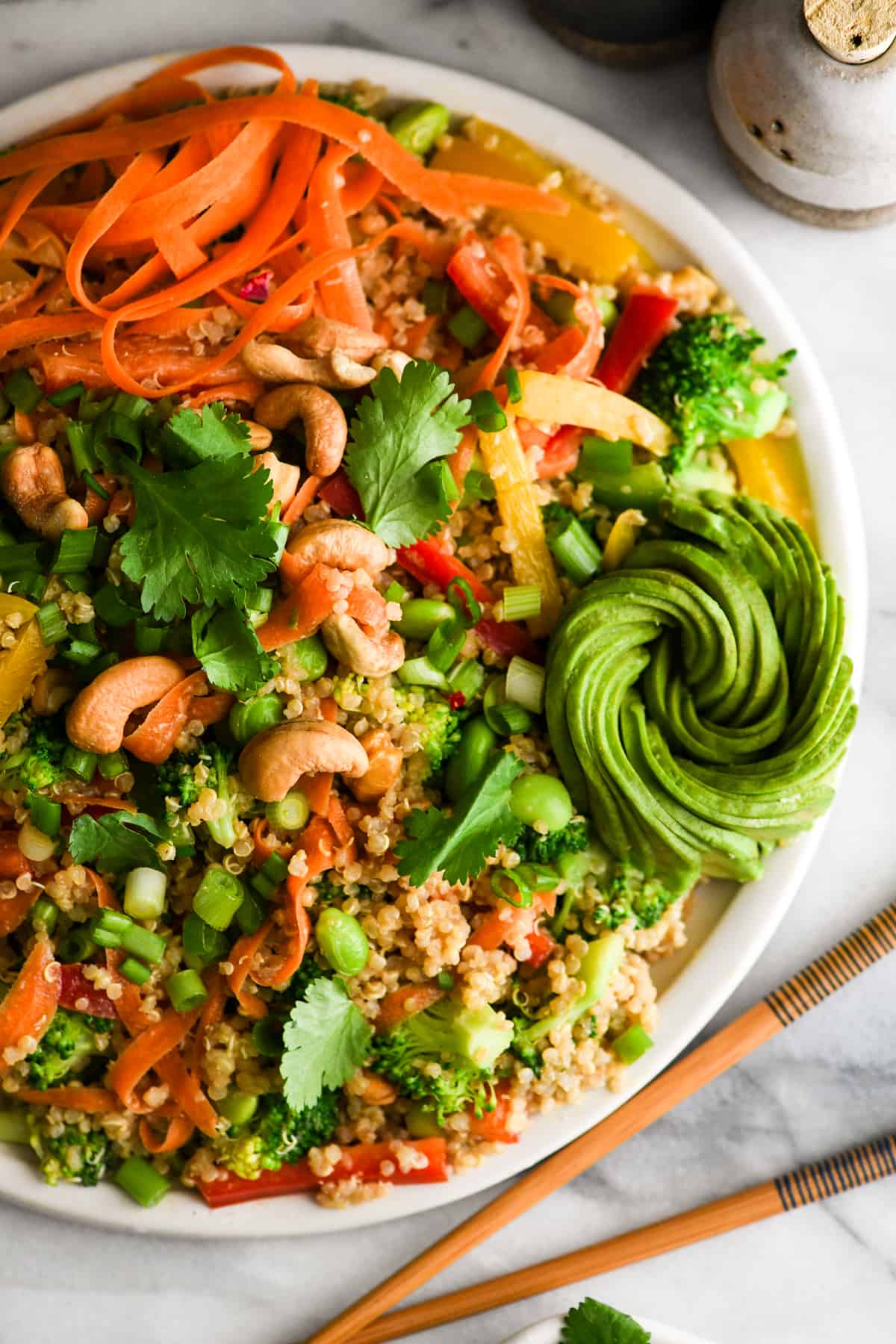 Overhead view of asian quinoa salad with peanut dressing on a round white platter with a gorgeous avocado rose 