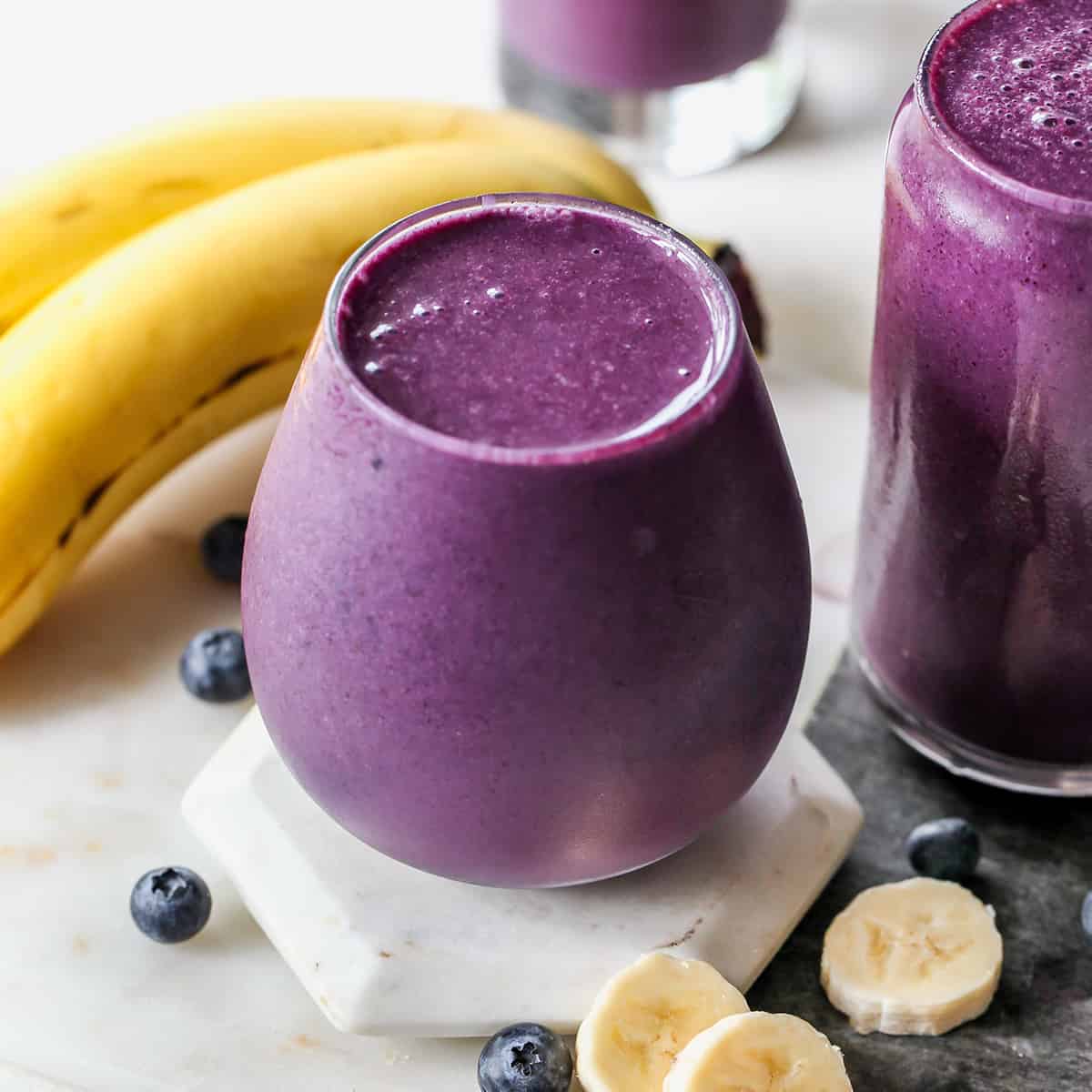 front view of a glass filled with blueberry smoothie with bananas and blueberries around it 