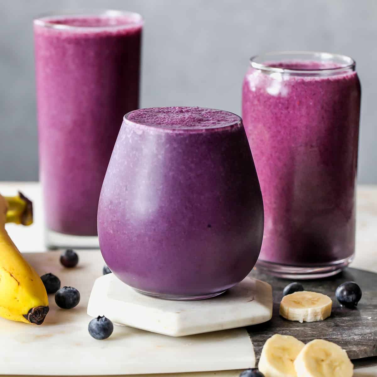 front view of three glasses filled with Blueberry Smoothie with bananas and blueberries around them