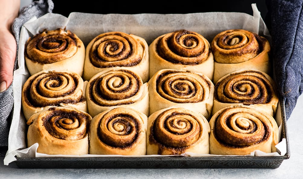 front photo of hands holding a pan of baked cinnamon rolls