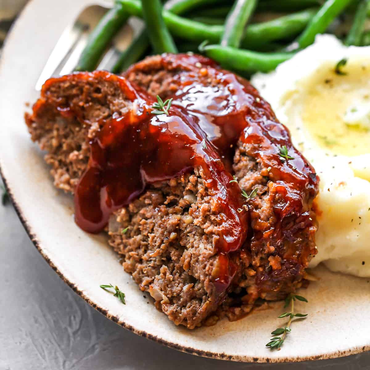 front view of two slices of the Best Meatloaf on a plate with beans and mashed potatoes