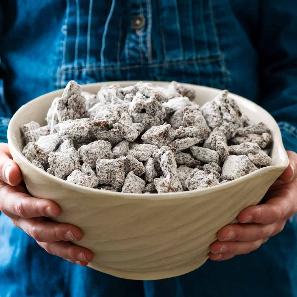 front view of hands holding a bowl of puppy chow (muddy buddies)