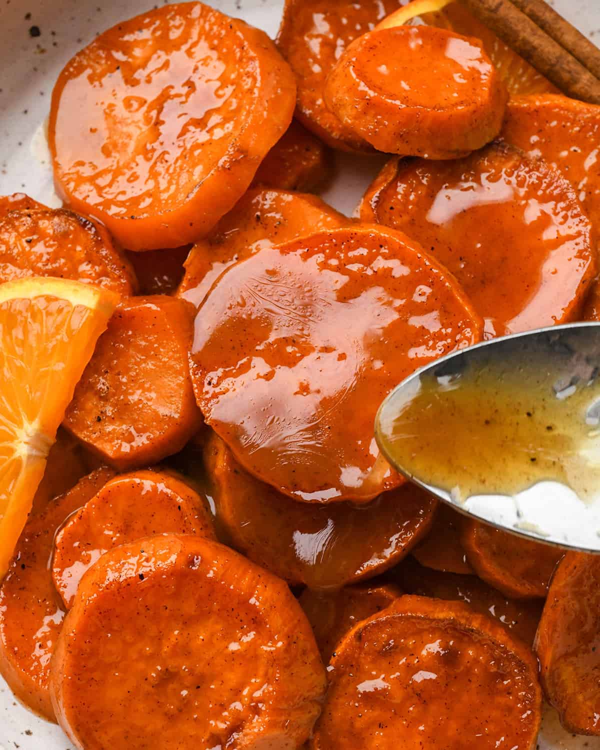 a spoon pouring sauce over Candied Yams on a plate 