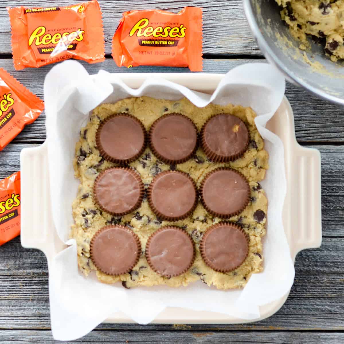 Overhead view of a baking dish with Candy Cookie Bars dough with three rows of three Reese's cups on top. 