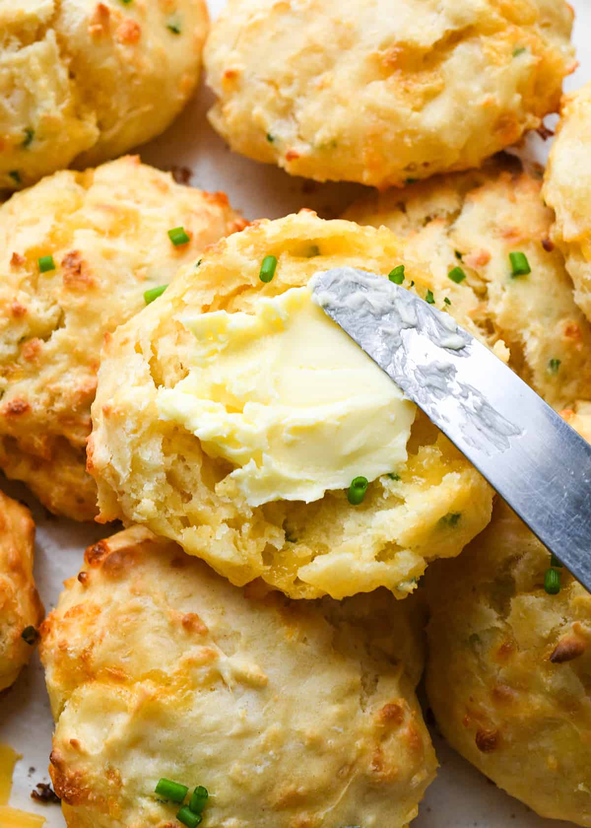 a knife spreading butter on top of a cheesy biscuit