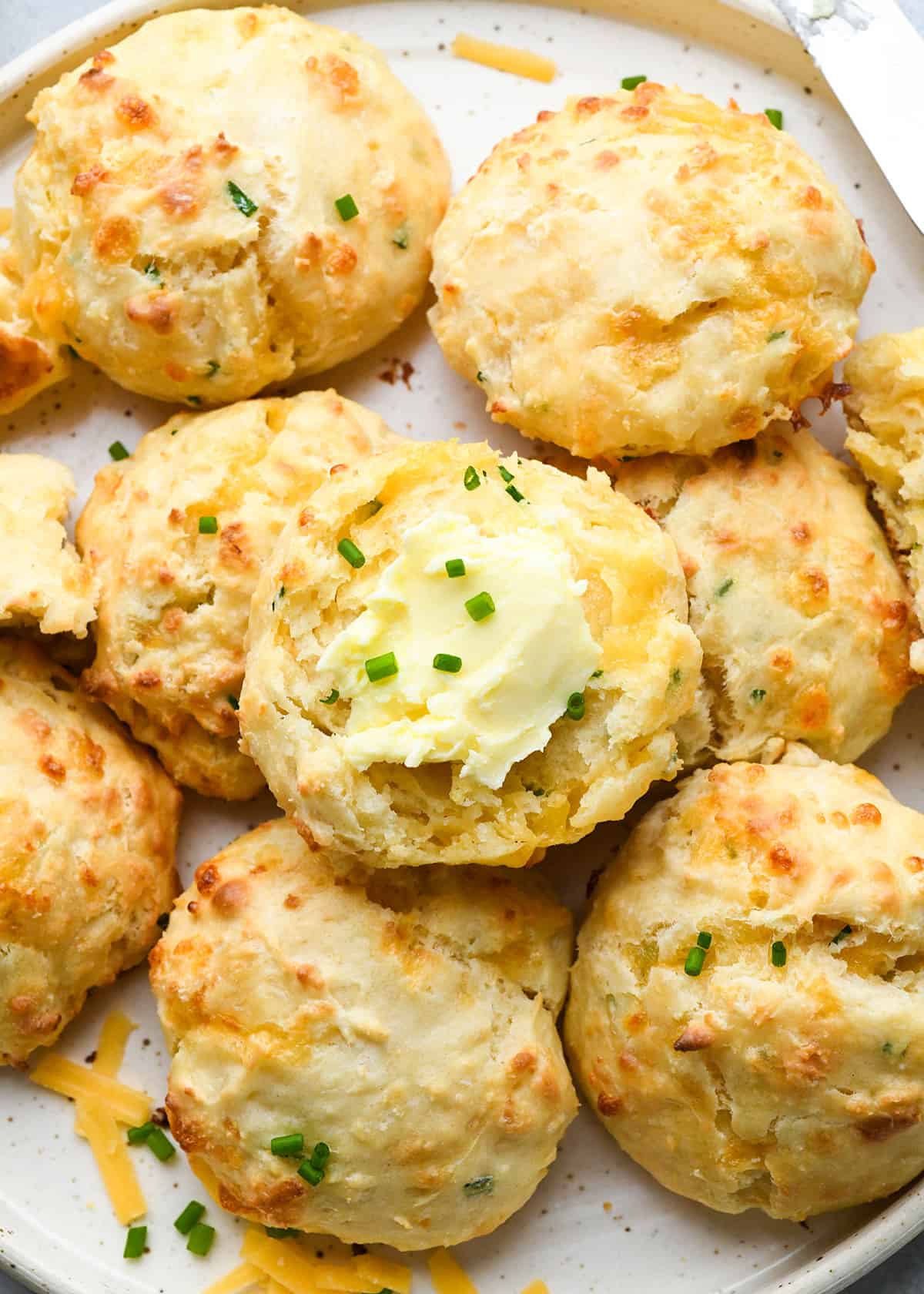 Cheese Biscuits on a plate, one cut in half with butter and chives on it