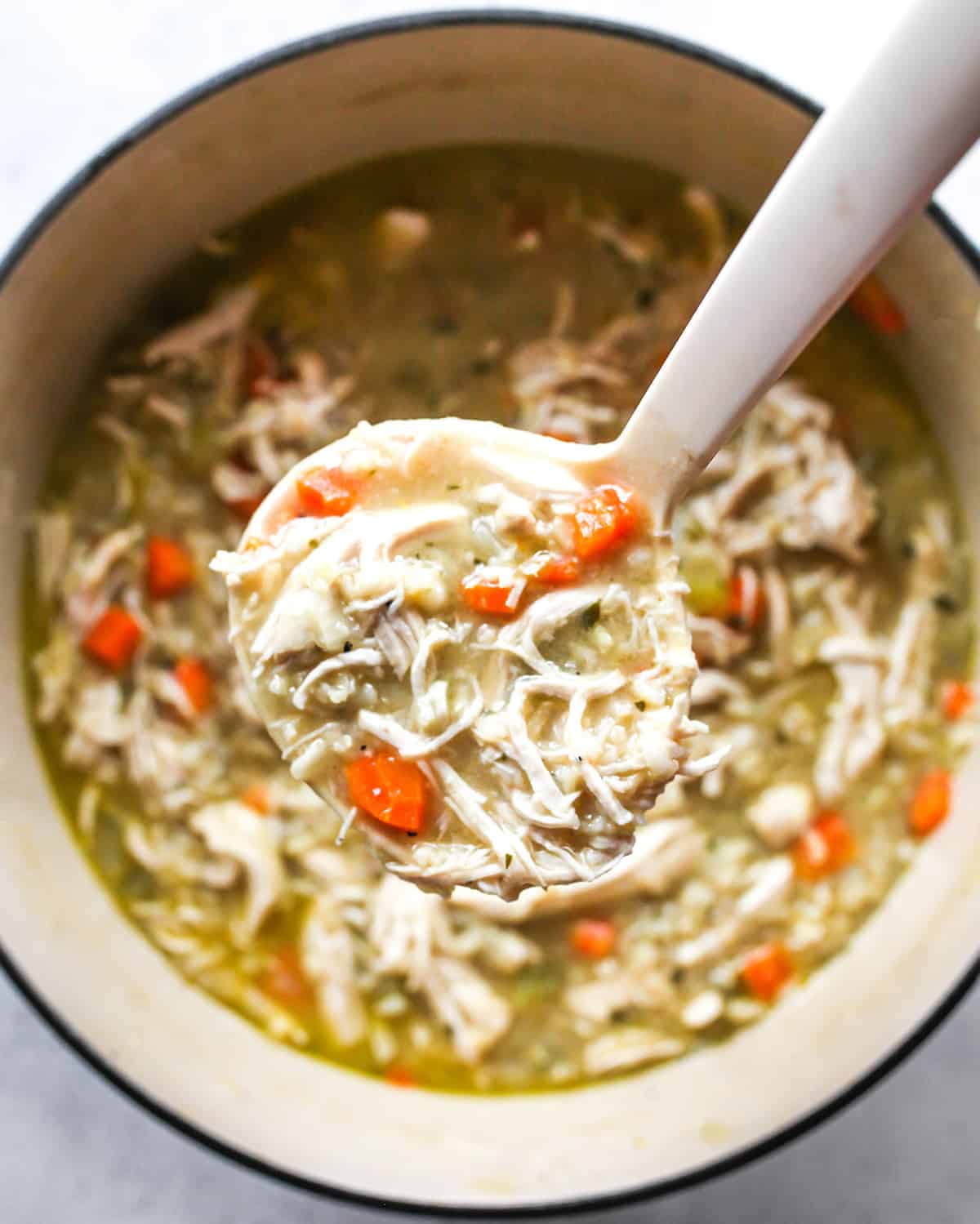 Overhead view of a ladle scooping chicken and rice soup out of a pot