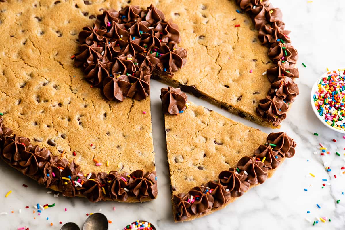 front view of a chocolate chip cookie cake with a piece cut out of it 