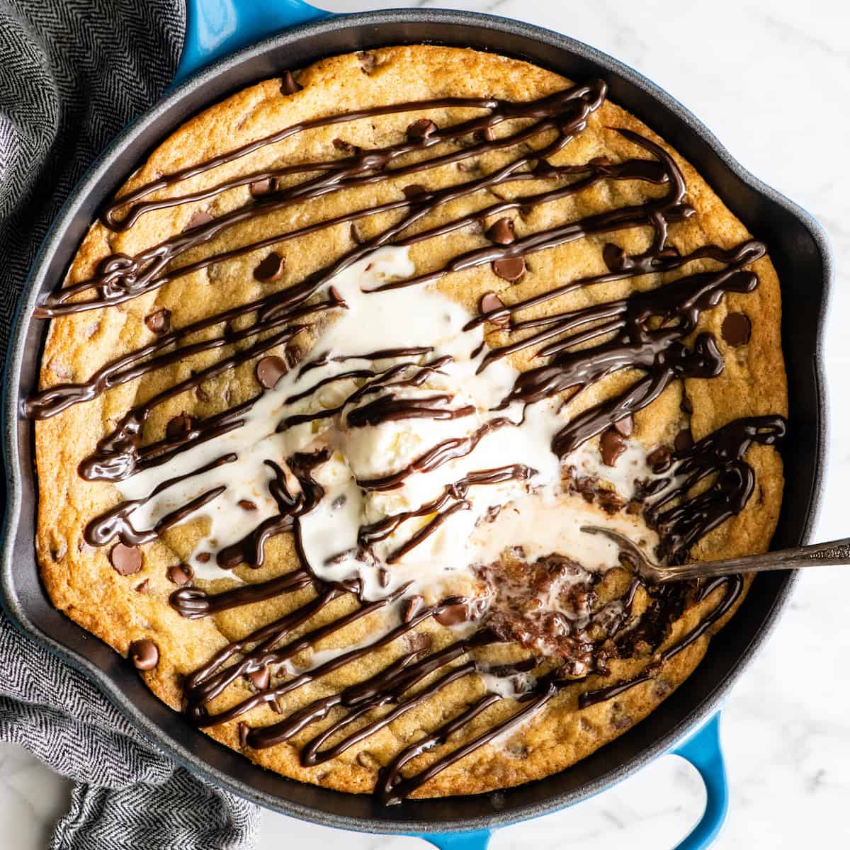 overhead view of a skillet cookie (pizookie) drizzled with chocolate topped with ice cream with a spoon taking a bite