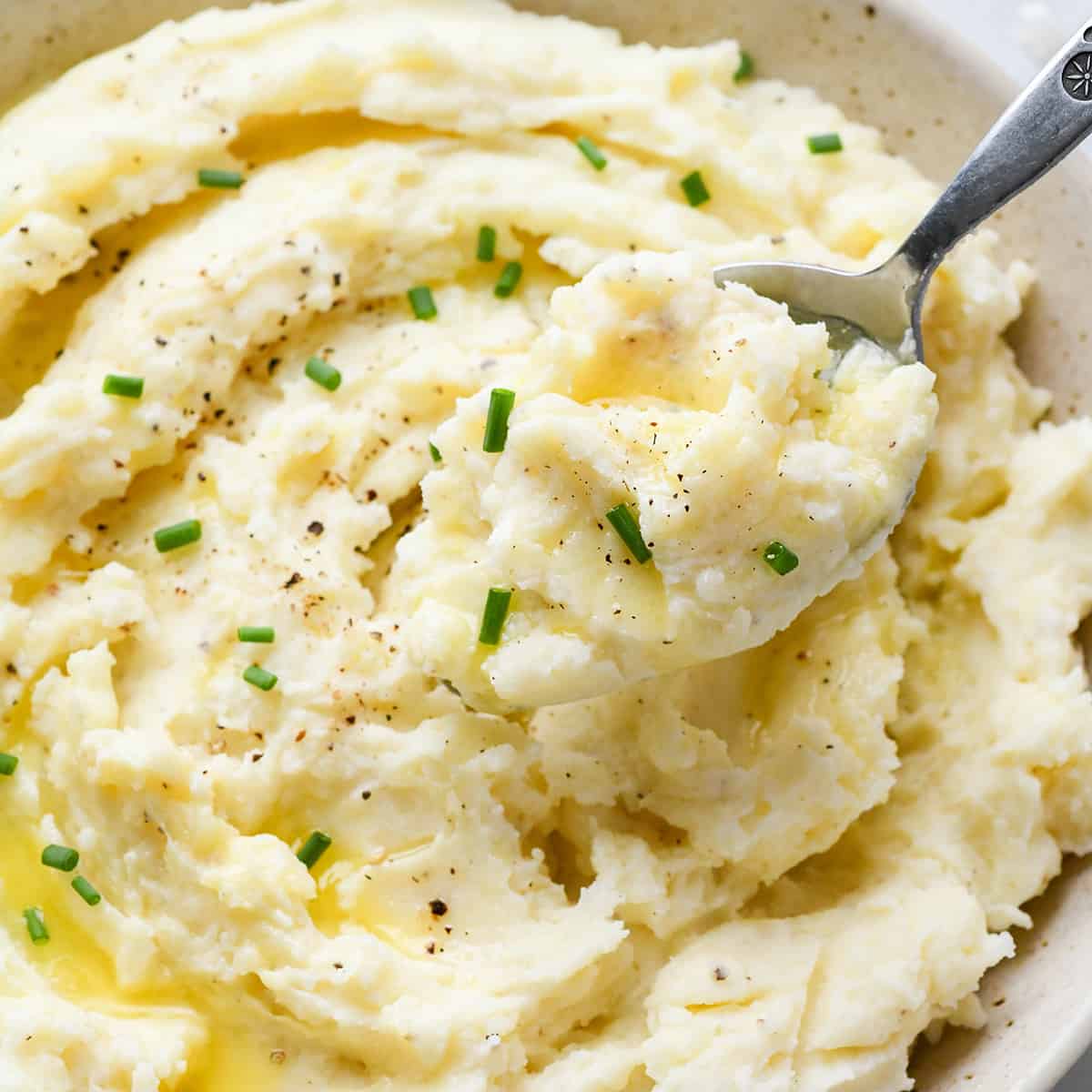 a spoon taking a scoop of Cream Cheese Mashed Potatoes out of a bowl. 