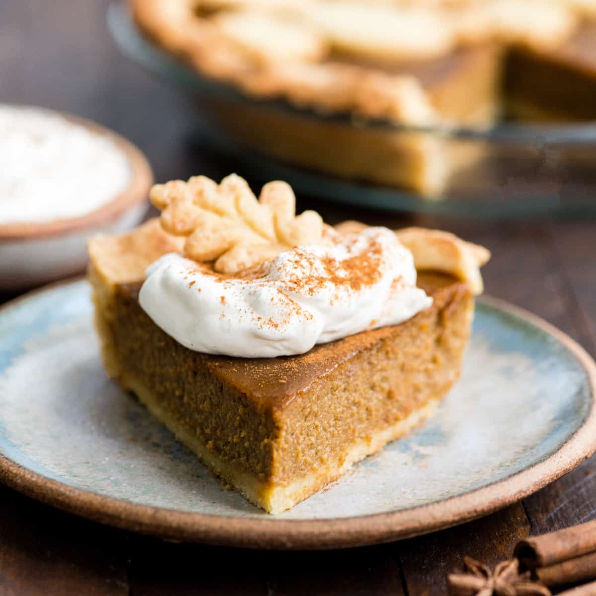 front view of a slice of dairy-free pumpkin pie on a plate with a dollop of whipped cream and a pie crust leaf on top