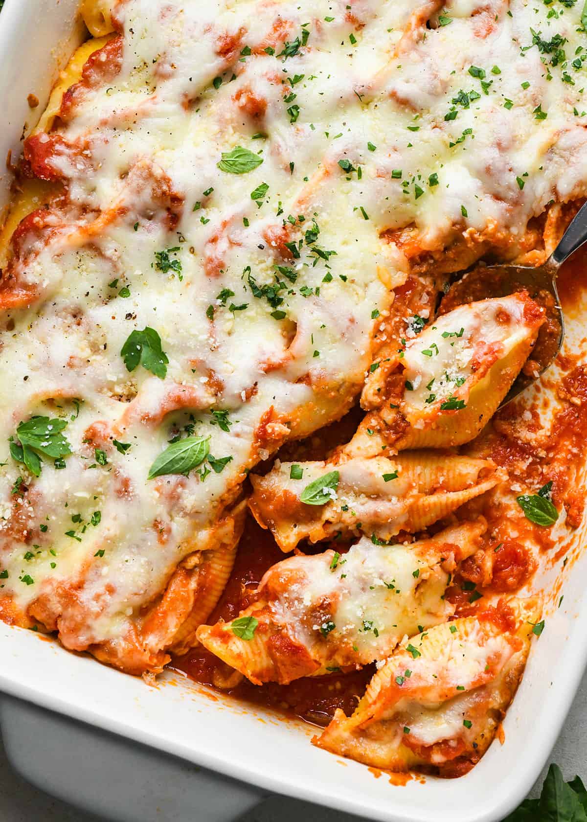 A spoon scooping Stuffed Shells out of a baking dish
