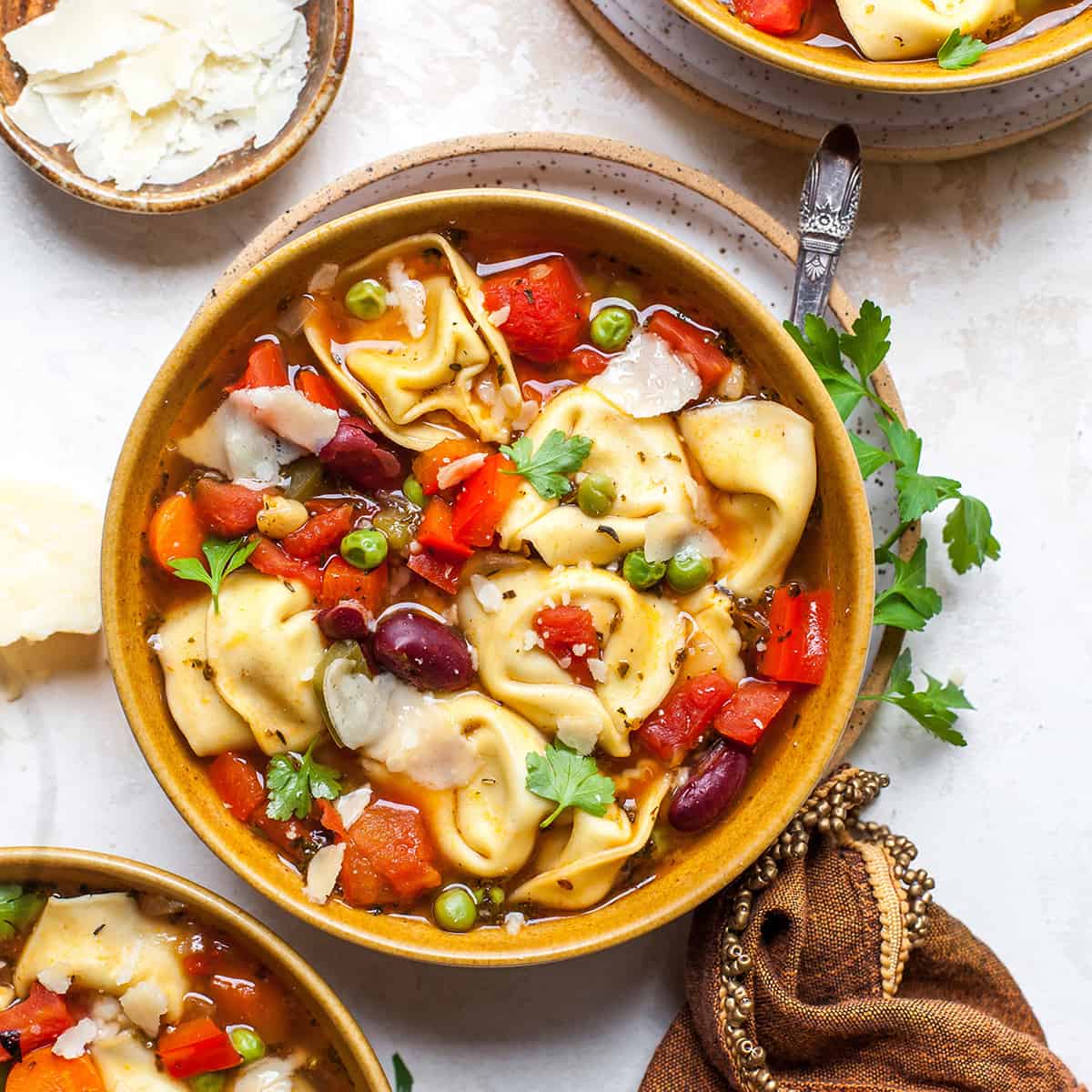 overhead view of a bowl of tortellini soup garnished with parsley and parmesan cheese