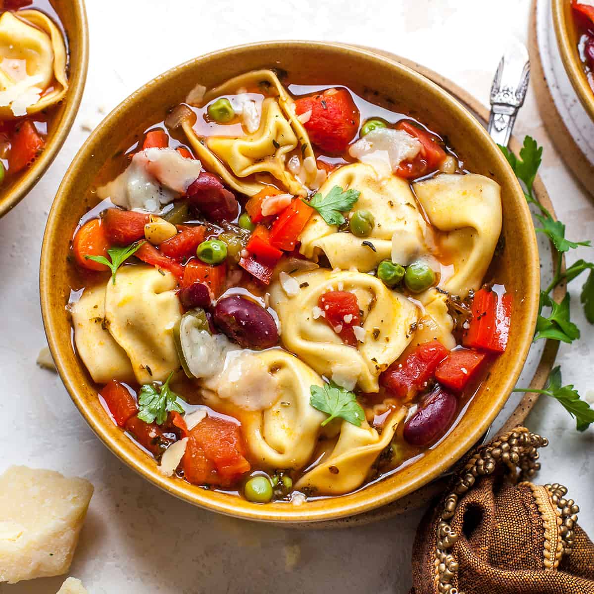 overhead view of a bowl of tortellini soup garnished with parsley and parmesan cheese 