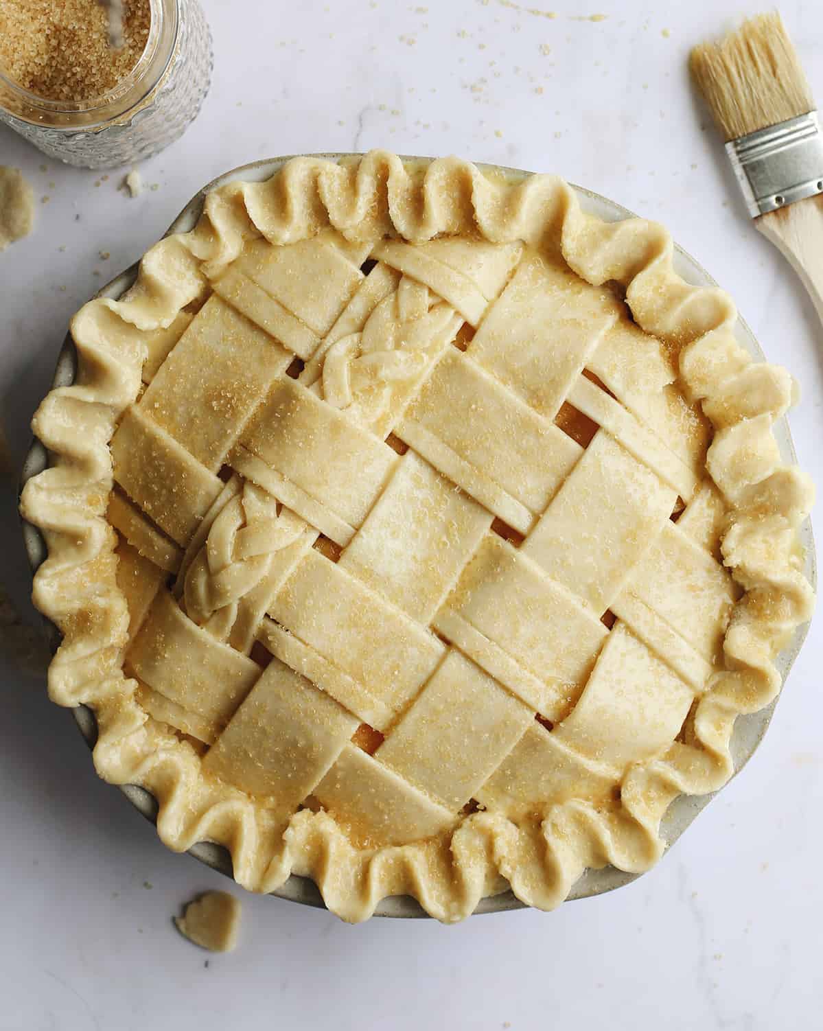 overhead photo of a Butter Pie Crust in a lattice pattern before baking with an egg wash and raw sugar