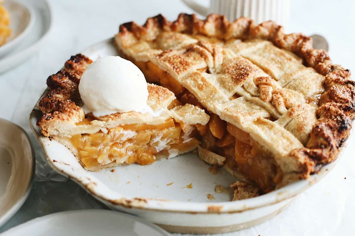 front view of a peach pie with a double Butter Pie Crust with a slice cut out and ice cream on top