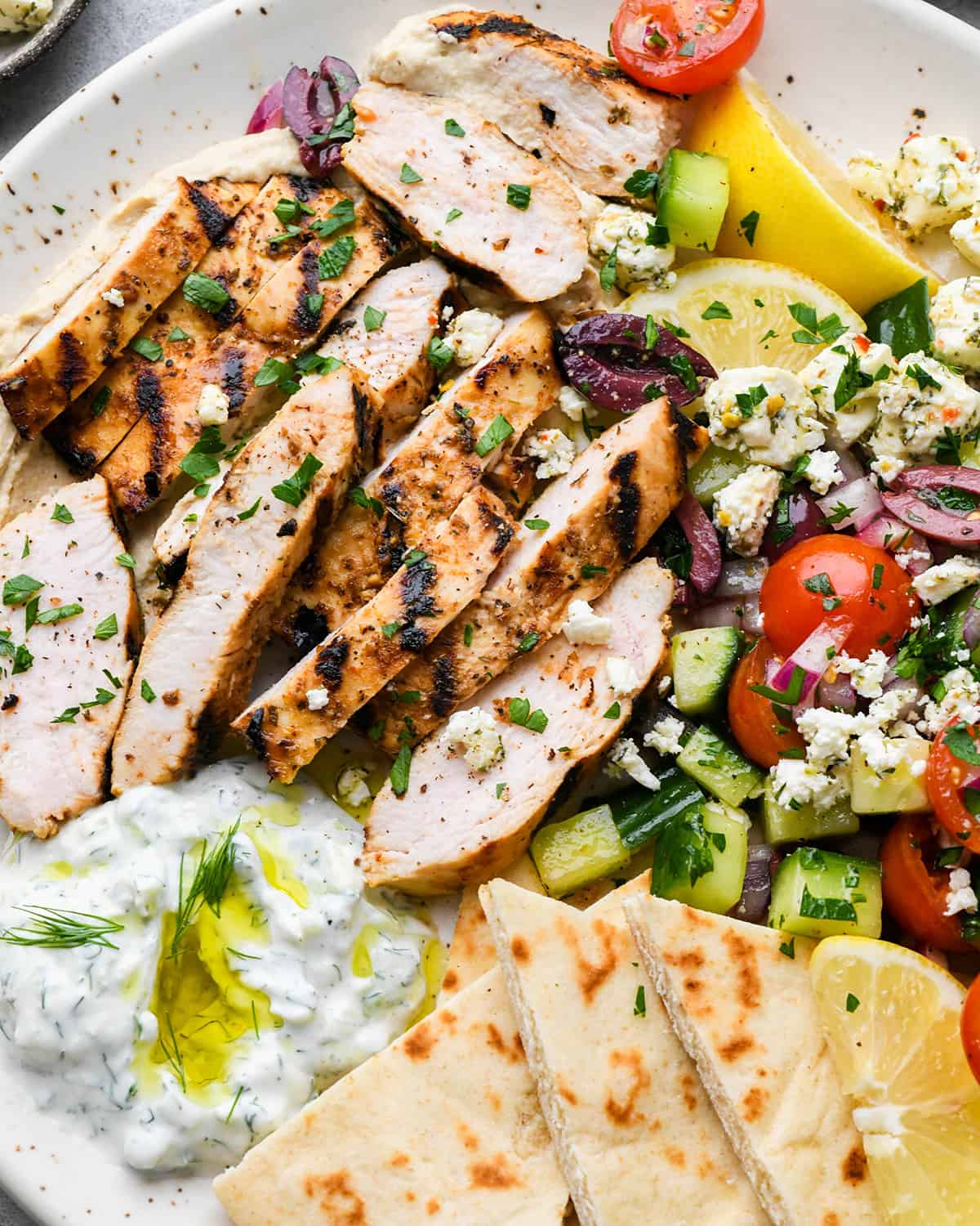 Greek chicken cut into slices on top of a greek salad