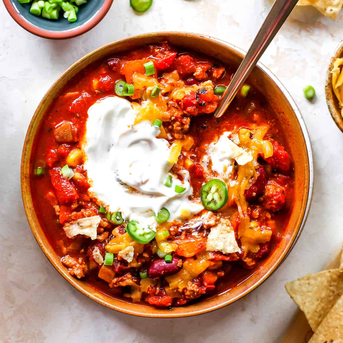 Overhead photo of a bowl of turkey chili with sour cream, cheese and green onions