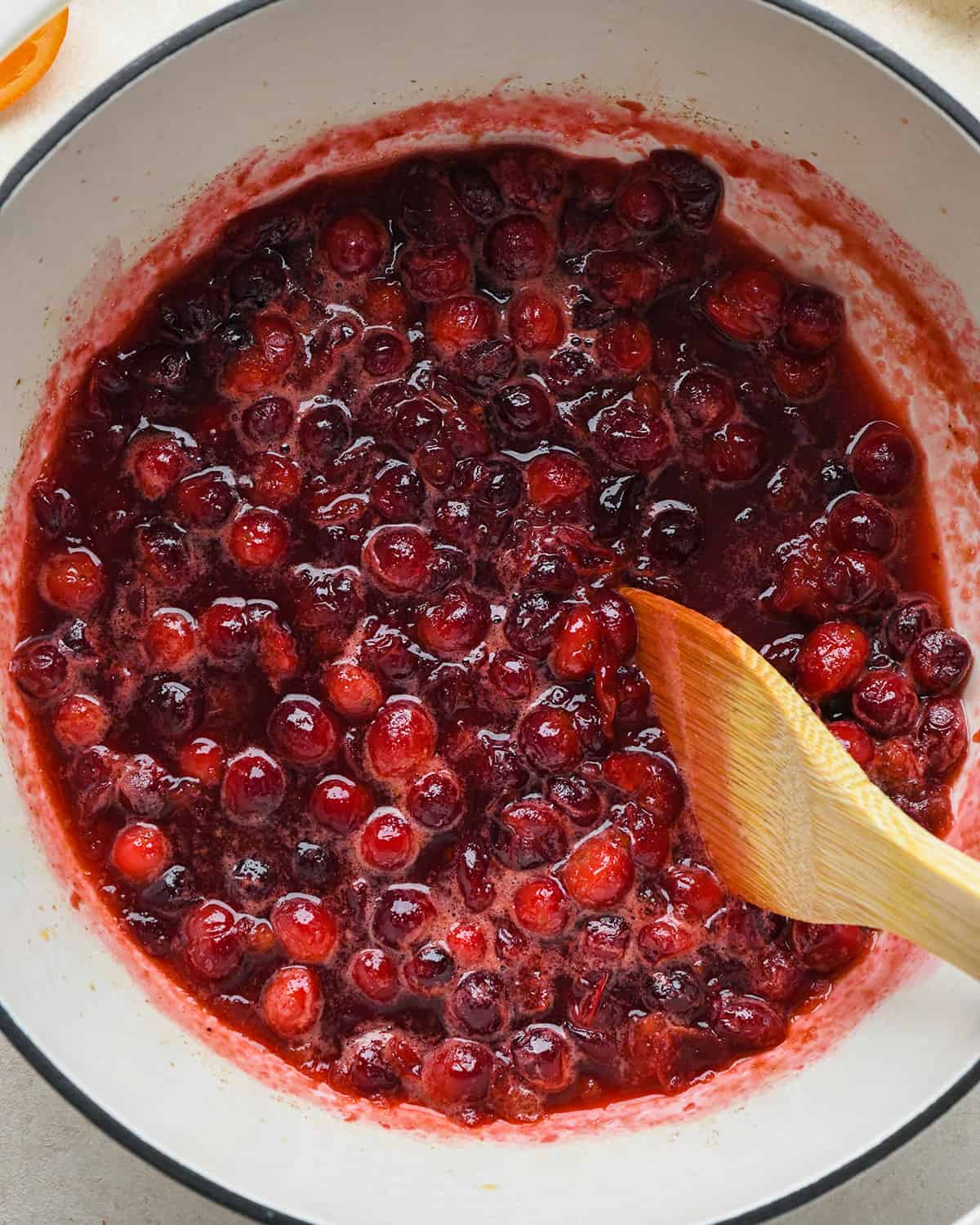 How to Make Cranberry Sauce - a wooden spoon stirring as the cranberries cook in a pot