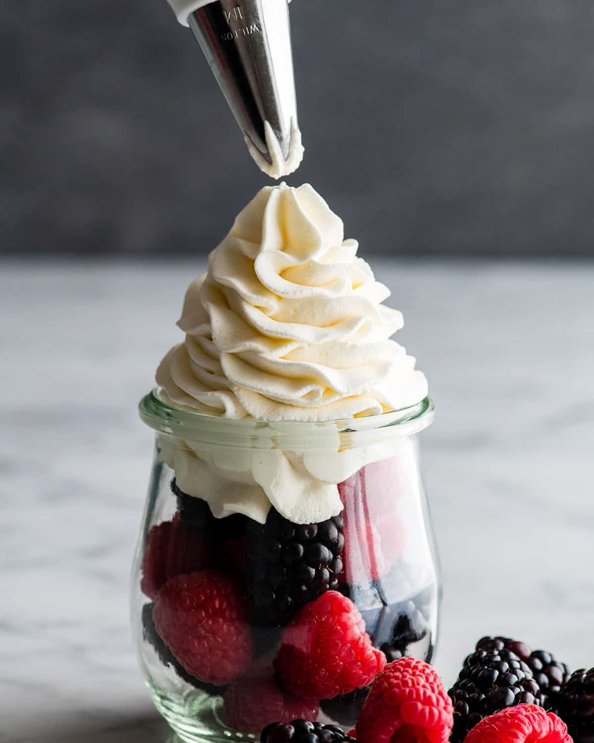 front view showing homemade whipped cream being piped over fresh berries