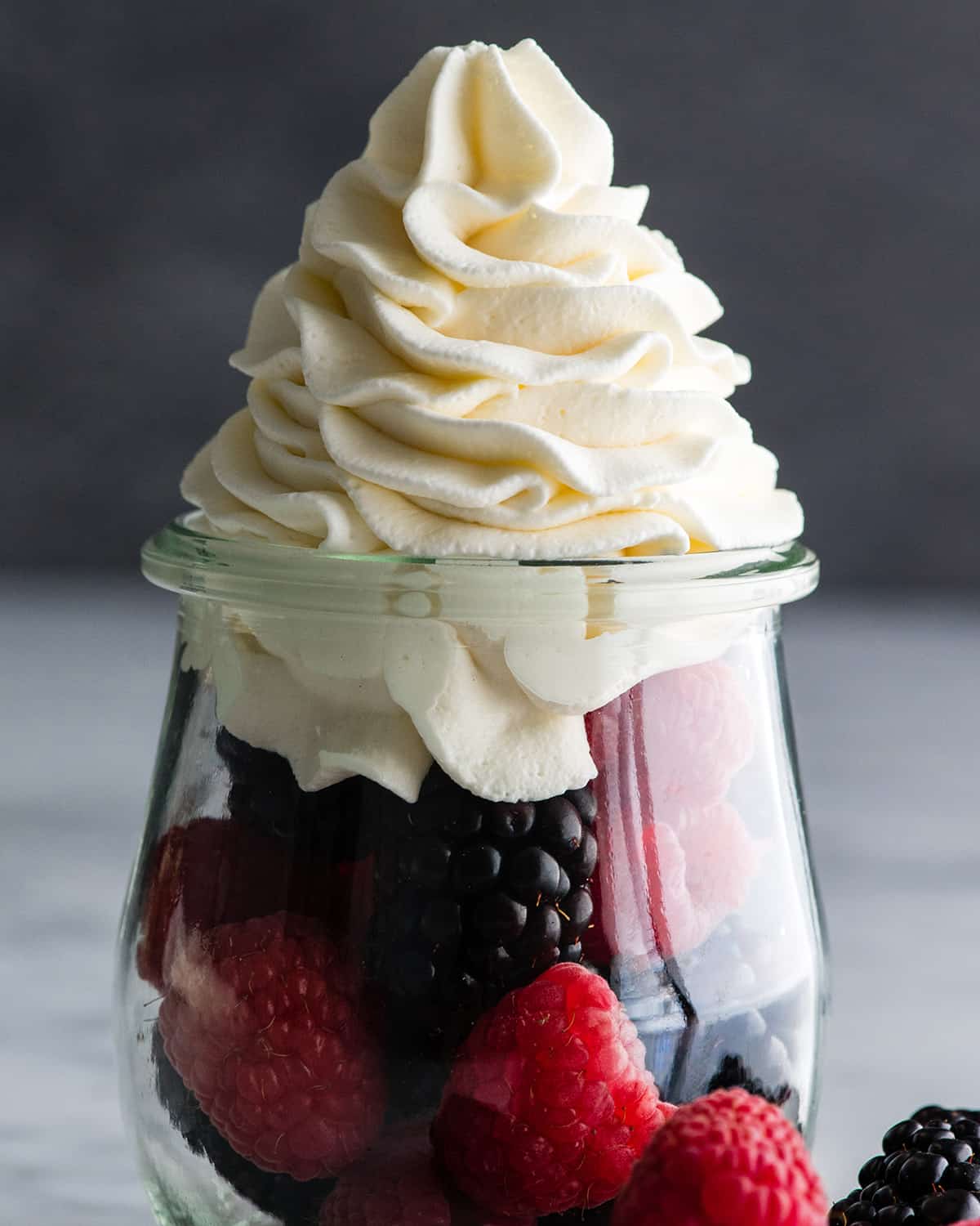 front view of homemade whipped cream on top of fresh berries in a glass jar