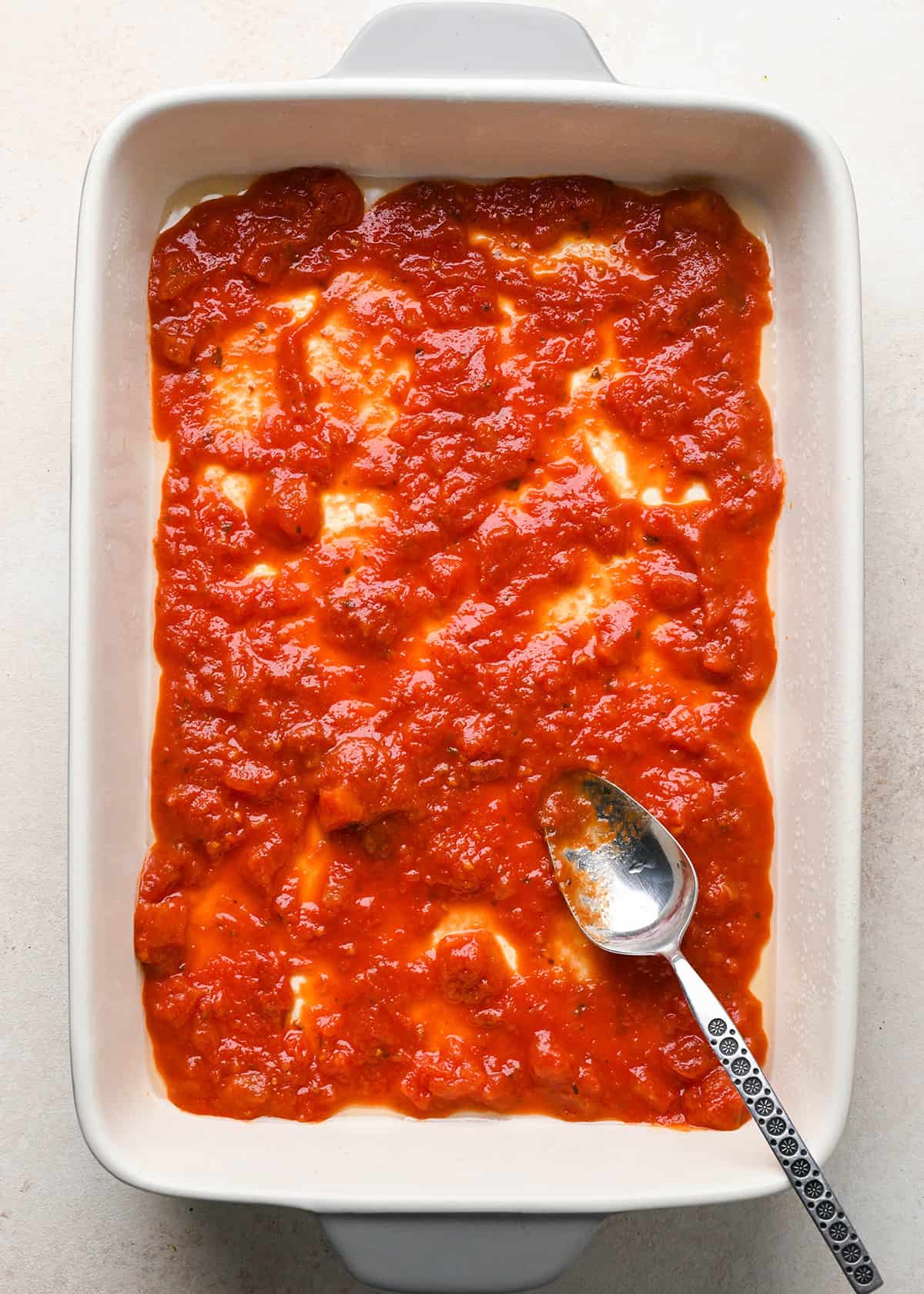 marinara sauce spread on the bottom of a baking dish