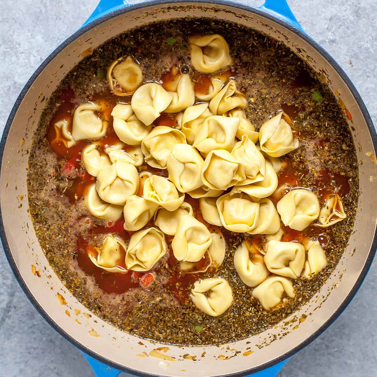 overhead photo showing how to make tortellini soup adding tortellini