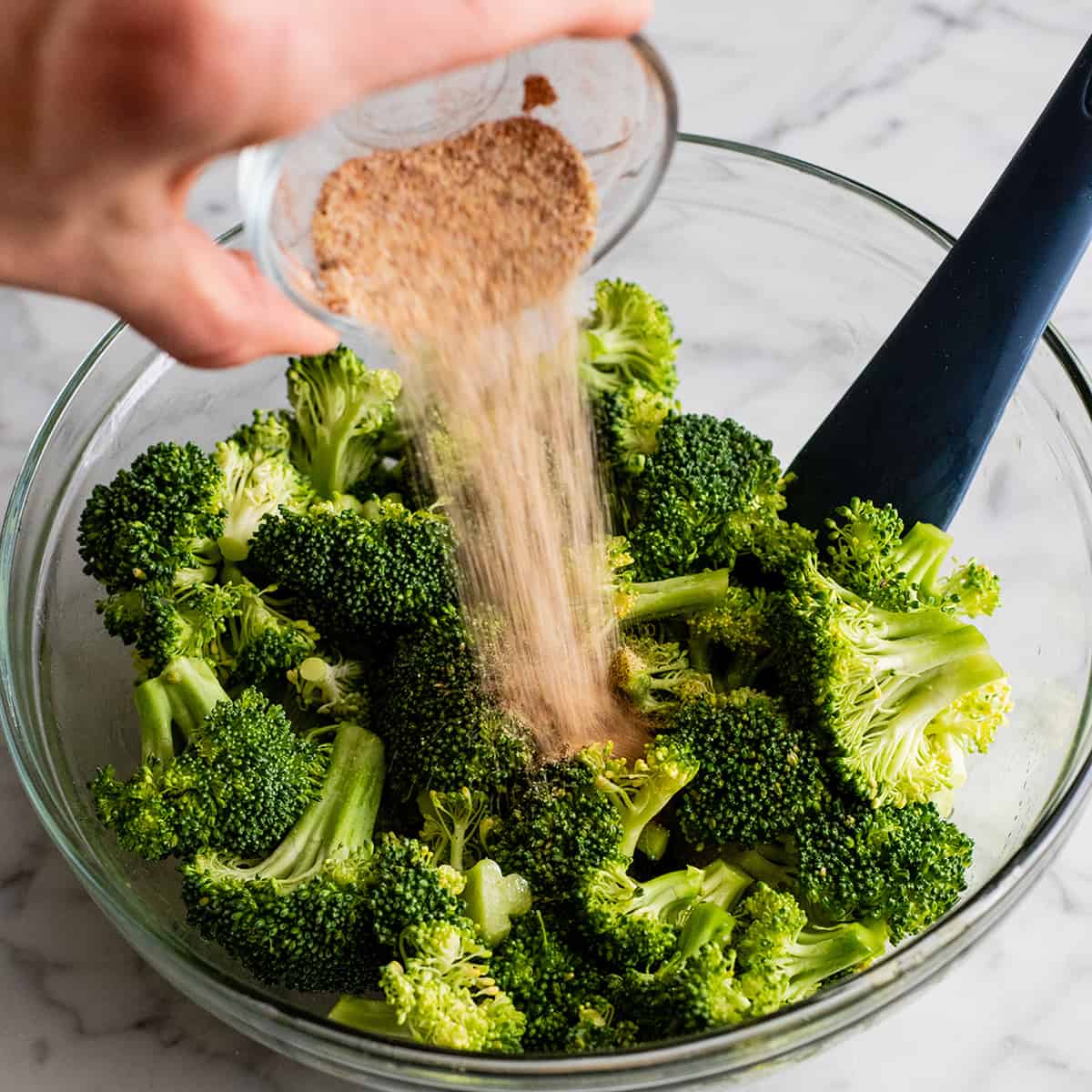 photo showing how to roast broccoli - pouring spice mixture onto oiled broccoli