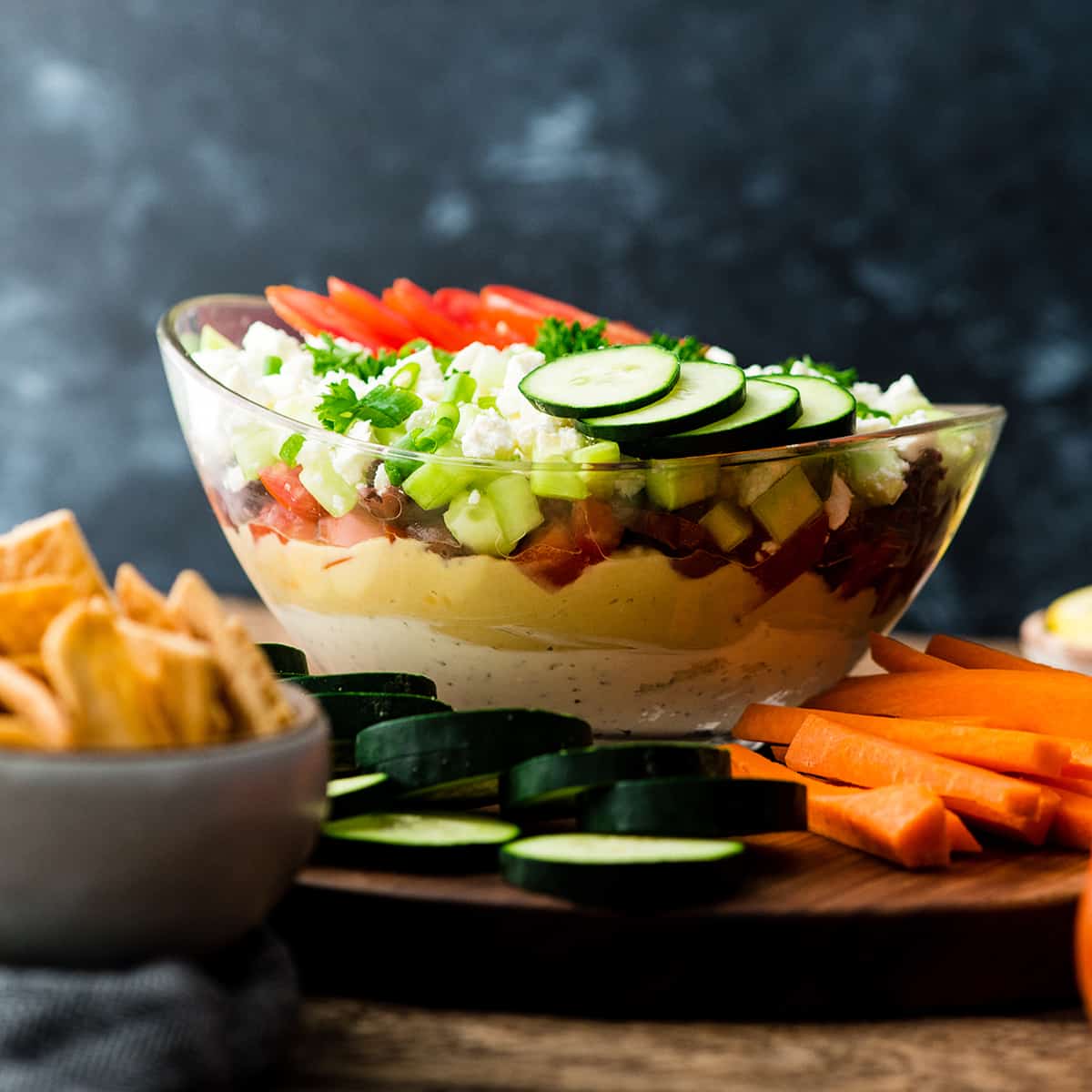 a bowl of layered Greek dip surrounded by veggies and pita chips