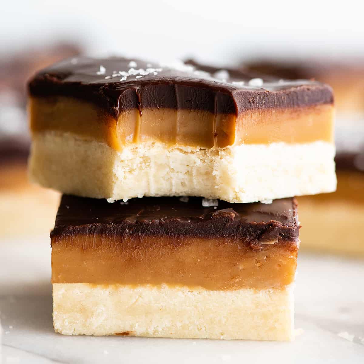 front view of two Millionaire Shortbread bars stacked on each other, the top with a bite taken out