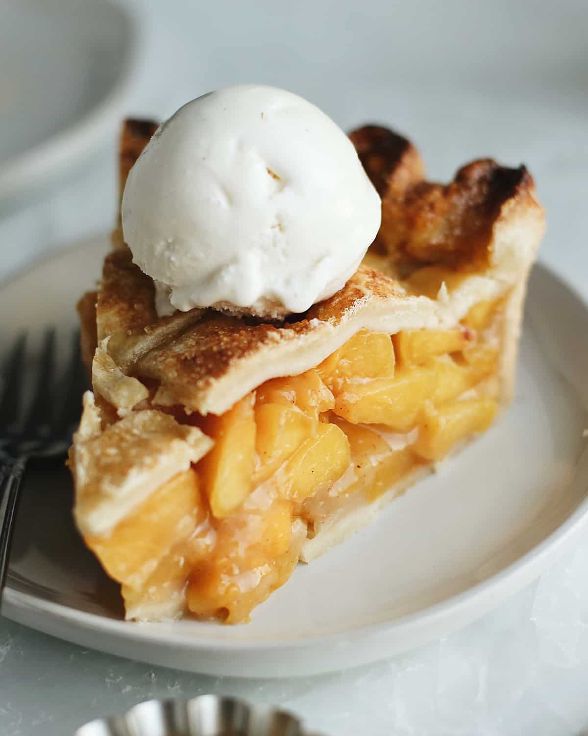 a piece of Fresh Peach Pie on a plate with a scoop of vanilla ice cream on top