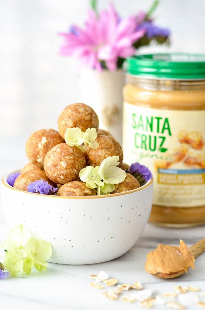 Side view of a bowl of Peanut Butter Oatmeal Balls with peanut butter and flowers in the background
