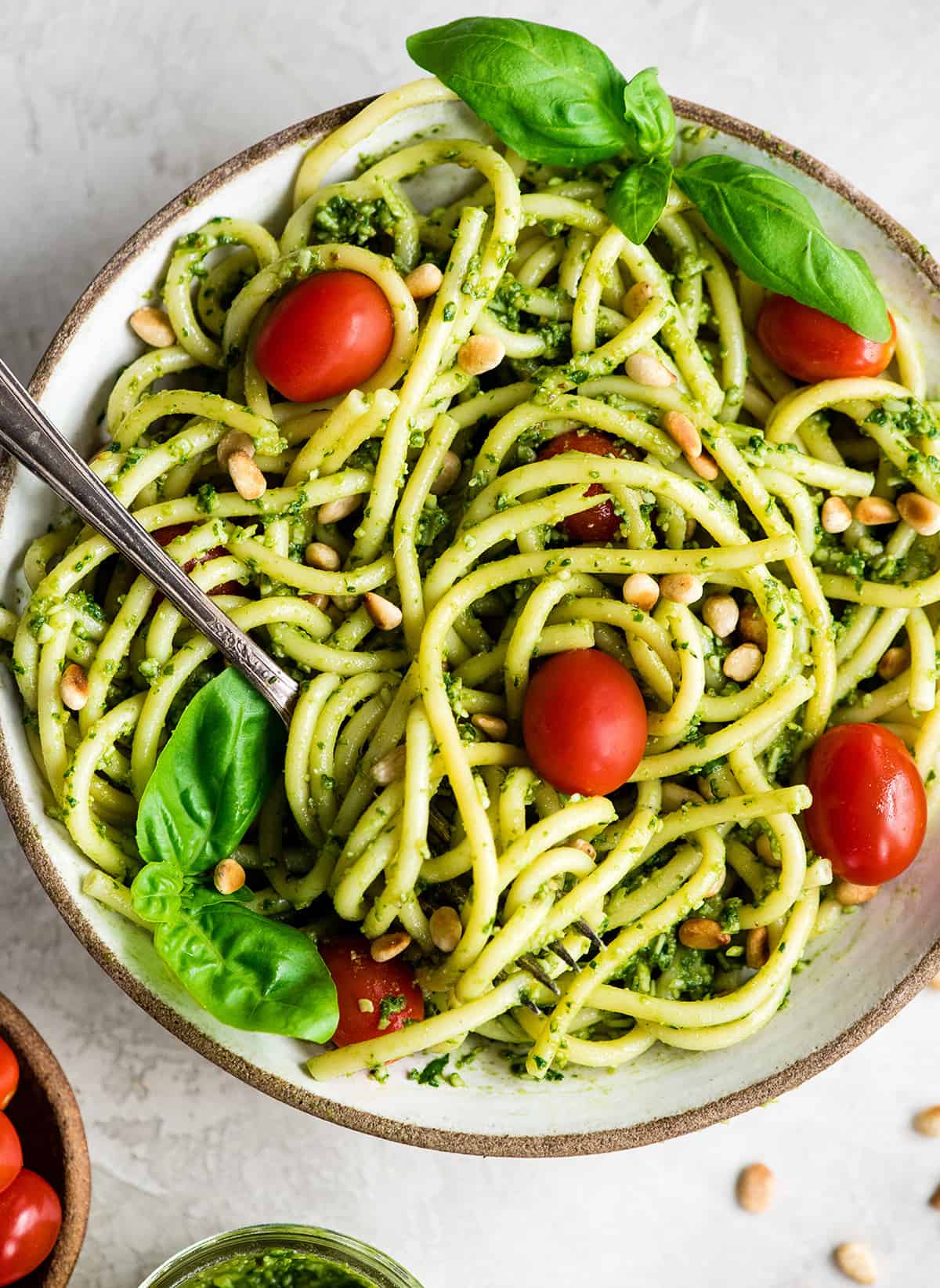 overhead view of a bowl of Pesto Pasta with tomatoes, fresh basil and toasted pine nuts and a fork with a twirl of pasta on it