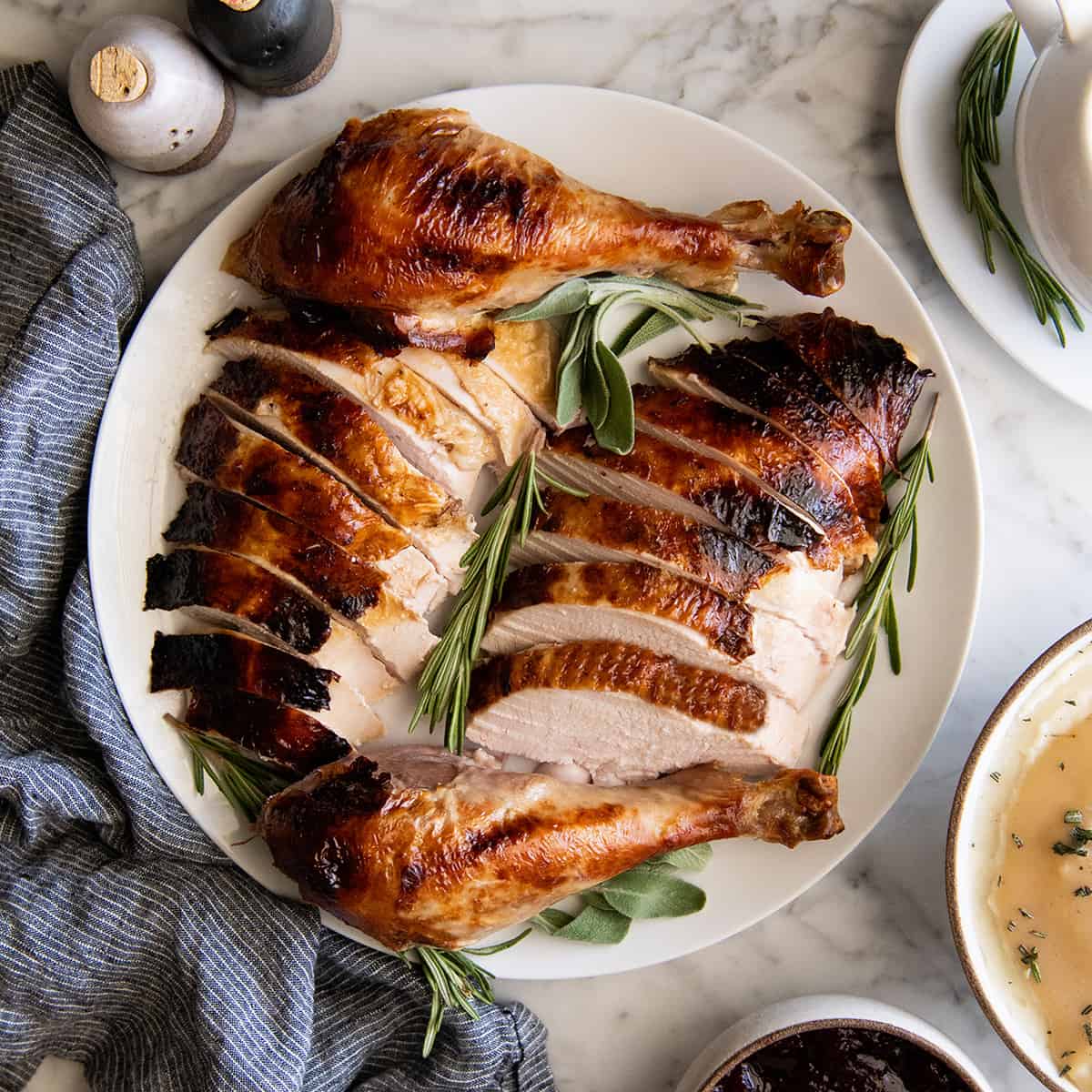 overhead view of roast turkey carved on a plate with herbs around it