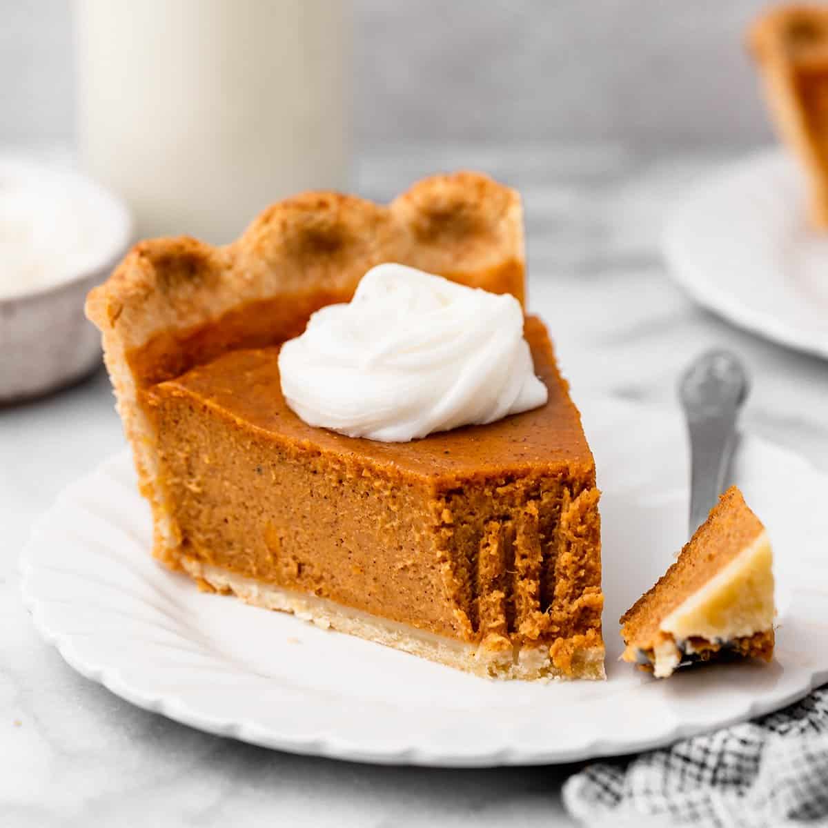 a slice of sweet potato pie with whipped cream & a bite taken out of it on a plate